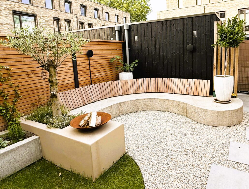 Modern en sfeervol tuinontwerp van een compacte achtertuin met een golvende betonnen designbank, staptegels in grind, een gazon en een houten eethoek.