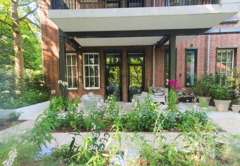 Gestort terrazzo terras met zitplek onder het balkon, grote border met pastelkleurige beplanting en witte verhoogde plantenbak