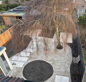 De aanleg van een organische achtertuin in Haarlem met Castle grind, keramische stapstenen en een grote bestaande boom.