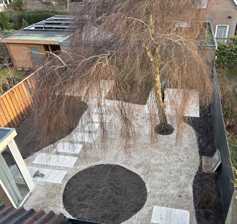 De aanleg van een organische achtertuin in Haarlem met Castle grind, keramische stapstenen en een grote bestaande boom.