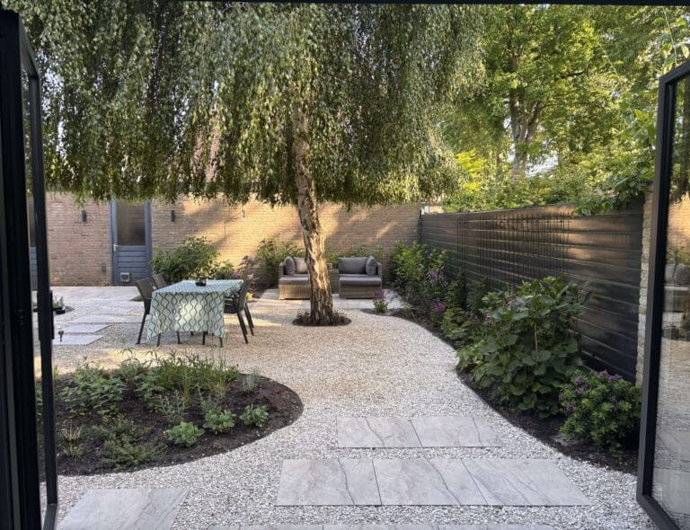 Zicht vanuit de woning op de opgeleverde Wabi-Sabi achtertuin in Haarlem met een natuurlijke flow en eettafel onder de boom.