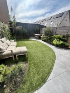 Foto van een aangelegde tuin met een gebogen gazon, grijze terrastegels, een loungebank en verhoogde borders van cortenstaal.
