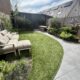 Foto van een aangelegde tuin met een gebogen gazon, grijze terrastegels, een loungebank en verhoogde borders van cortenstaal.