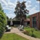 Overzicht van een loungeterras met groene meubels, een slingerend pad van Padvast, gazon en de houten uitbouw van de woning.
